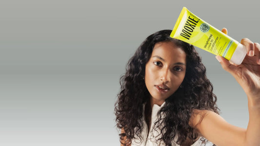 A woman with wavy hair applying haircare products in a bright bathroom, showcasing a nourishing routine.