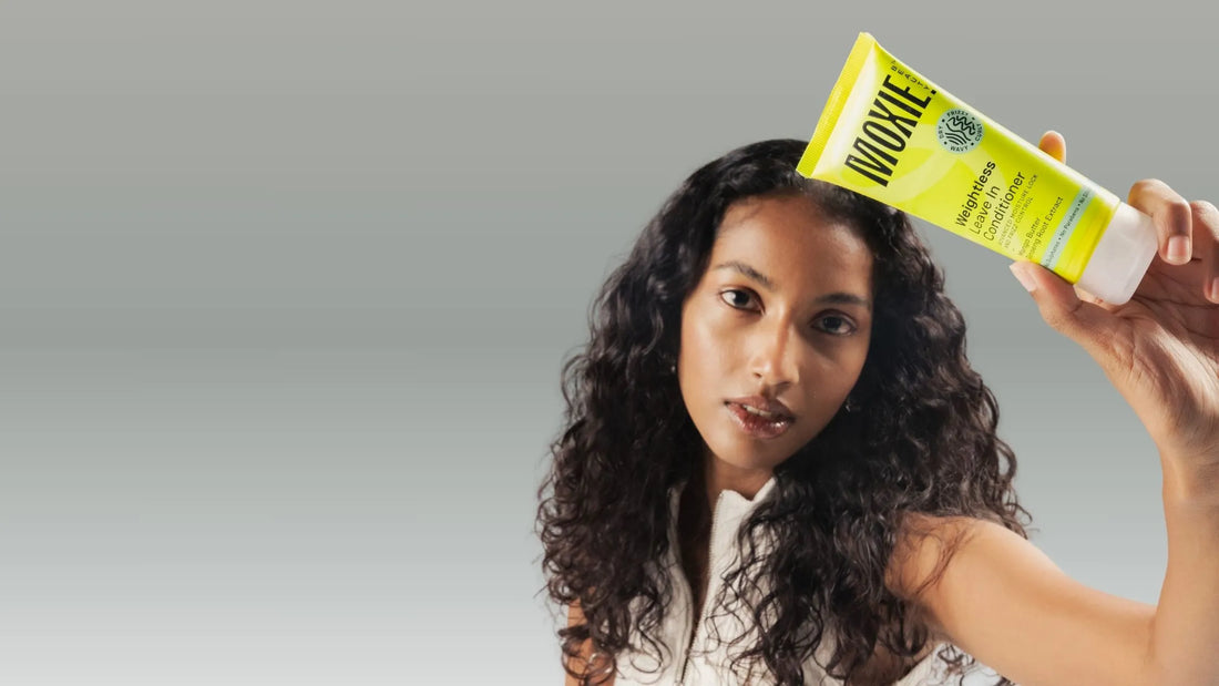 A woman with wavy hair applying haircare products in a bright bathroom, showcasing a nourishing routine.