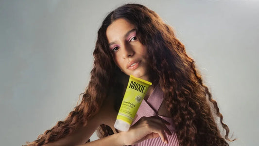 A woman with beautiful curly hair applying hair product for care and styling tips.
